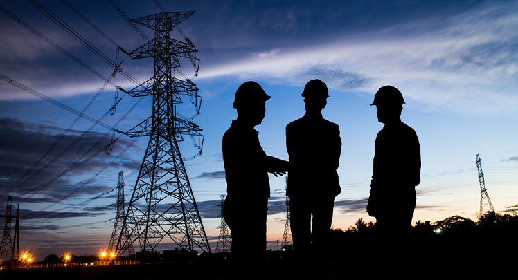 Silhouettes of three men standing in front of power lines at dusk.