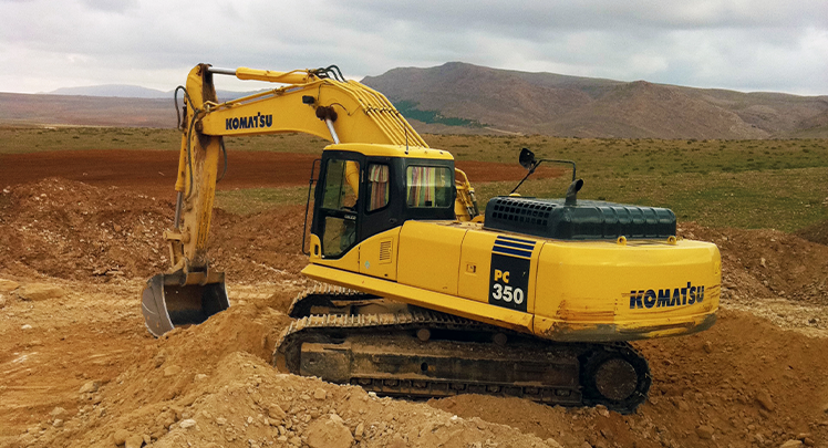 A yellow excavator in a dirt pit.