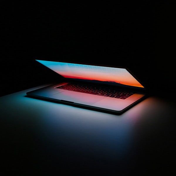 A laptop with a colorful screen lit up in the dark.