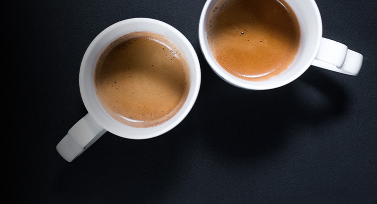 Two cups of coffee on a black surface.