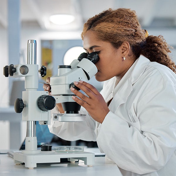 A woman in a lab coat looking through a microscope.