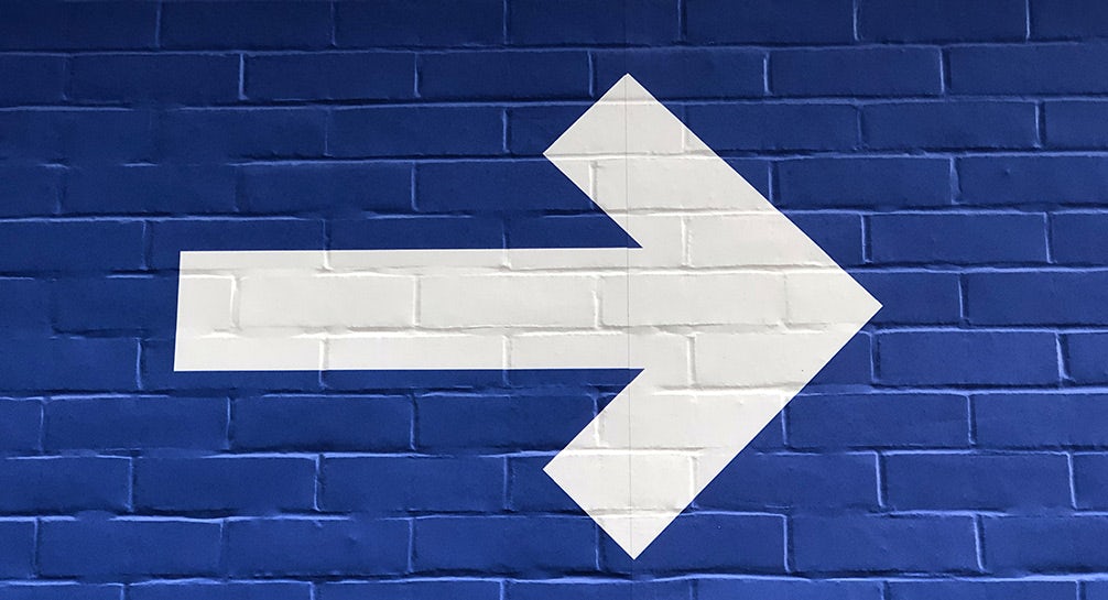 A white arrow on a blue brick wall.