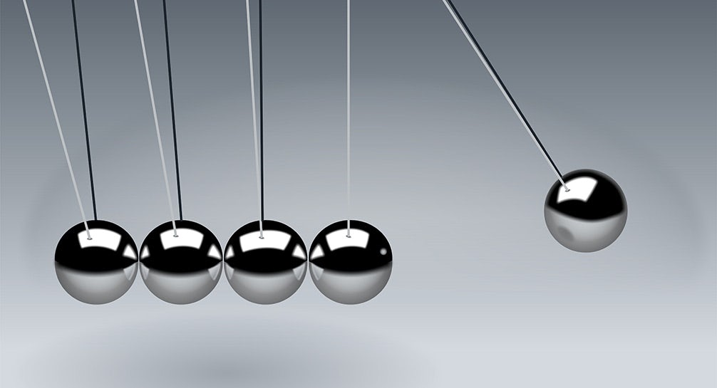 A set of metal balls hanging from strings on a gray background.