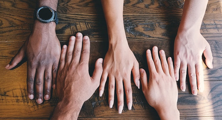 A group of people holding hands on a wooden table.